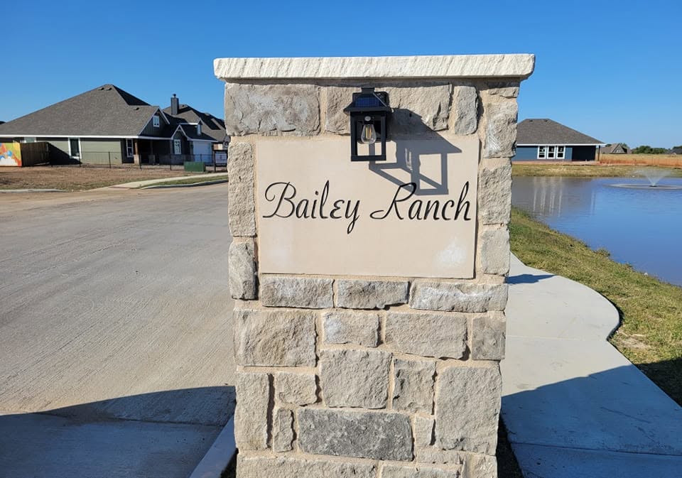 Stone entrance sign reading Bailey Ranch, with neighborhood homes and a pond behind it.
